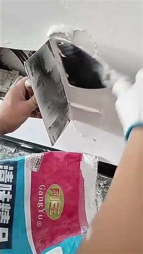 worker uses a wide putty knife to apply white plaster to a wall