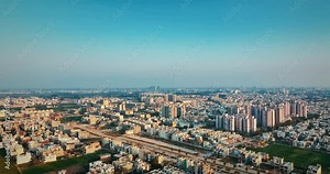 Hovering above urban structures, a drone moves towards the horizon, capturing Mohali city at sunset with a blue sky and yellowish buildings creating an amazing hue.