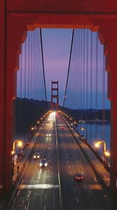 Vertical video of the Golden Gate Bridge at night. Inspirational drone flight through red tower above busy traffic road. Cinematic pink cloudy sunset over San Francisco bay on background, California