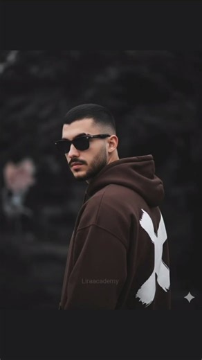 ‎آکادمی لیرا | هوش مصنوعی | بیزینس کوچ‎ on Instagram‎: "کپشن بخون🦢🤍 @liraacademy . برای دریافت متن و لینک سایت کافیه پیج رو فالو کن دایرکت کلمه ( متن ) رو ارسال کنی "A young man (without any changes to his face or hair from the reference photo) wearing classic Wayfarer-style sunglasses. He is standing in a semi-profile position, slightly looking towards or gazing at the camera. He is wearing a dark chocolate hoodie, and the prominent feature of his clothing is a large white logo 