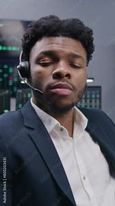 African American financial analyst works at computer with displayed real-time stocks, turns and looks at camera. Colleagues analyze exchange market charts at background. Investment concept. Portrait.