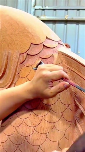 carving intricate fish scale patterns into a large wooden sculpture using a sharp metal chisel