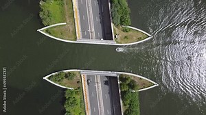 Aerial top down view of modern aqueduct or water bridge is constructed to convey watercourses across gaps showing a sailboat moving over the infrastructure and vehicles cars driving under 4k
