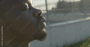 Side close-up portrait of the handsome confident african man looking forward, closing his eyes and enjoying the sunny weather. 4k footage.