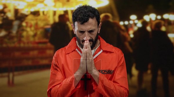 Hispanic man in orange prison jumpsuit with beard prays at a fairground carousel, juxtaposing incarceration with the vibrant festive setting Stock Video Footage - Alamy