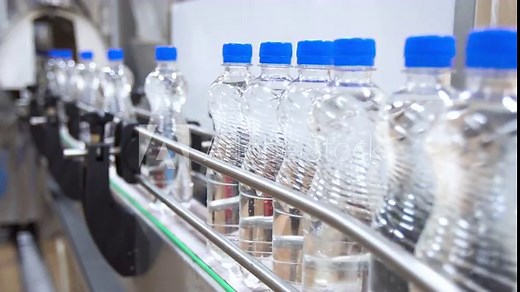 Production and bottling of carbonated water in plastic bottles on automatic conveyor on industrial plant. Clear plastic bottles with blue caps on a conveyor belt. Manufacturing of bottled drinks.