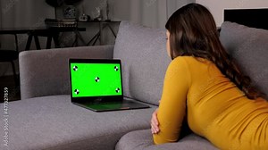 Green screen laptop woman student watching online remote master class lesson course. Back view beautiful female looks computer display with mockup chromakey, lying on couch at home. Distance education Stock Video