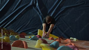 A young handsome dark-haired male climber trains on a climbing wall indoors. Getting ready and mentally adjusted, gaining strength to start climbing the climbing wall and begins to move. 4k footage