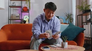 Planning budget. Rich happy asian man counting money cash use smartphone calculator application, calculate domestic home bills. Guy satisfied of income earnings, win, saves money for planned vacation
