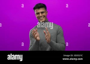Young man clapping happily in glasses and sweater against vibrant pink background exuding joy and charisma Stock Video Footage - Alamy