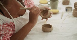 Young African American woman at a clay food grade pottery workshop in a light studio. A close-up of the hands of a woman who is shaping a piece of clay in her hands for her future product.