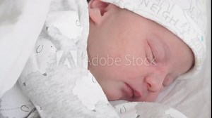 Close-up the face of a newborn baby in the first days of life who shudders, smiles and stretches through a dream. A newborn baby grimaces through a dream. Newborn baby in the first minutes of life.