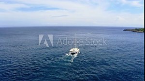 Catamaran boat sailing in blue sea waters along coast of Bali.