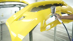Man with protective clothes and mask painting car using spray compressor ,yellow front bumper
