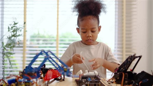 Focused African American young girl building a DIY robotic arm. Little engineer connecting wires on a STEM educational project at home. Child learning robotics, coding, and technology skills.