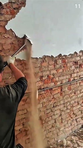 Chipping plaster off brick wall using gloved hands