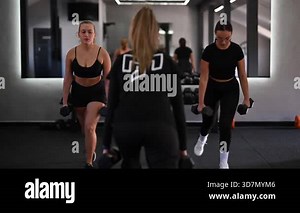 Three women engage in a strength training workout in a modern fitness studio. They focus on proper form while lifting dumbbells and maintaining motivation.