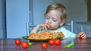 Happy sweet child making a mess in the kitchen while eating spaghetti. Funny toddler child with home made pasta and tomato sauce