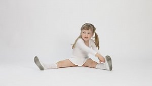 Pretty little girl sitting on the floor and doing exercise, white background
