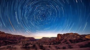 Download Long exposure shot of star trails forming circular patterns in night sky above desert landscape. Night sky timelapse with rotating stars, astrophotography for free