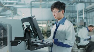 On High Tech Factory Asian Engineer Uses Computer for Programing Pick and Place Electronic Machinery for Printed Circuit Board Surface Mount Assembly Line. Production of PCB with SMT Machinery.