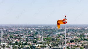 Wind direction indicator on background of city landscape. Air sleeve moving in the wind near helicopter landing place site. Orange wind sock. 4K