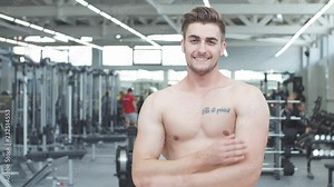 Attractive shirtless blond male bodybuilder indoors in well-equipped gym, showing muscular torso and ripped abs
