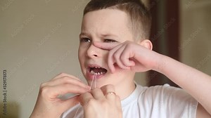 a mother loosens and tries to pull out a baby tooth to a small child boy using dental floss.