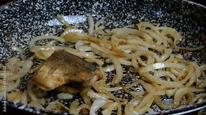 White sliced with half rings onions, fried until golden brown, in frying pan on vegetable oil to caramelize. Floured sea white fish, hake or pollock. Close up.