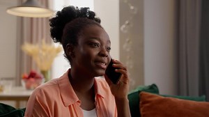 Serious African American business woman female ethnic lady girl businesswoman homeowner model client hold mobile phone talking cellphone call smartphone conversation speaking sitting couch indoor home