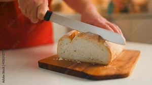 Cutting with a knife crusty bread in modern kitchen, delicious bread lies on a wooden cutting board