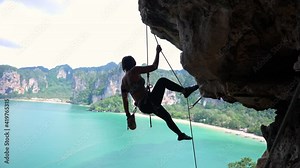 Confidence Asian female climber with safety hanging rope climbing on rocky mountain at tropical island. Healthy strong woman enjoy outdoor active lifestyle and extreme sport in summer holiday vacation