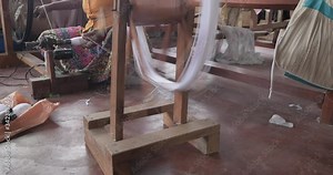 Hands of an old woman using an old spinning wheel to turn wool into yarn