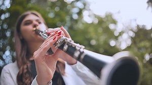 A girl plays the clarinet in the park in the summer.
