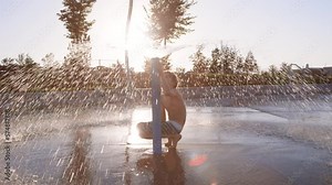 9 year old boy under giant splash pad water sprinkler, observing how it works