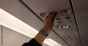 Woman hand on air conditioner control panel overhead in airplane. Passenger changes air conditioner intensity during flight slow motion