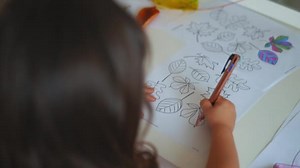Little girl coloring different types of leaves on a paper sheet with a pen