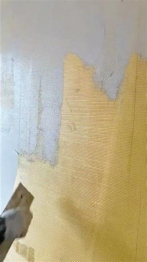 Applying a thin layer of plaster over a yellow mesh grid on the wall