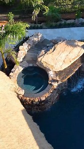 This pool has it all: featuring a massive grotto, elevated hot tub, upper and lower pools, and not one but two Tiki Huts. A true backyard paradise. #insanepools #lucaslagoons #backyarddesign | Lucas Lagoons