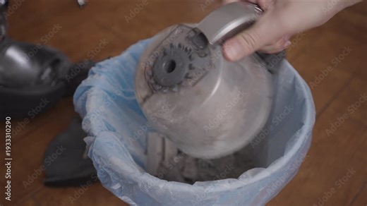 Process emptying vacuum cleaner dust container into trash bag, discarding household dirt and debris, maintaining home hygiene and cleanliness.