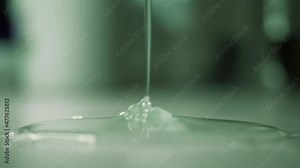 Liquid soap or dish gel dripping onto table. Thick liquid glue slowly pours in thin stream from above and spreads over surface. Close-up from side. Unknown dangerous chemical substance spills on floor