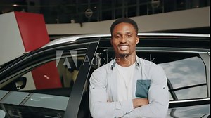 African american car dealership principal standing in vehicle showroom. Own Car. Overjoyed African American Man While Standing In Dealership Center, Happy Black Guy Celebrating Purchasing Vehicles.