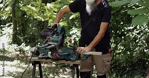 Carpenter making slow cross cut on wood plank using miter saw, close-up