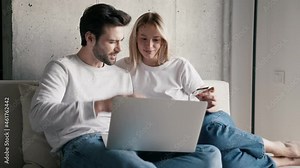 Positive couple entering bank card number on laptop and talking