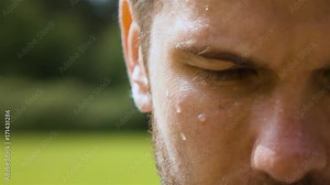 Epic extreme close-up shot of sweaty man outdoor in park. Drop of water on his face macro slow motion. Turning head from dowm to camera