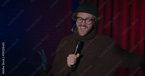 Talent show concert. A young comic guy with microphone makes performance on stage. Male entertainer talking jokes for audience. Comedy show preparation on gradient light background