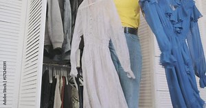 Girl decides which dress to choose. Front view, woman stands against an open wardrobe and tries on two dresses that she holds in her hands.
