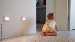 A curious infant in a lion-print onesie explores the terrazzo flooring of a bright, modern home, with wall lights adding a warm ambiance to the adventurous scene.