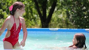 Three children whirl and fall in swimming pool in summer garden