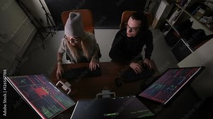 Male and female hackers working on computers with data code on display screens in a dark room. HD.